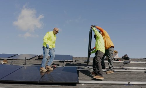 Three workers dressed in yellow installing solar panels on a rooftop